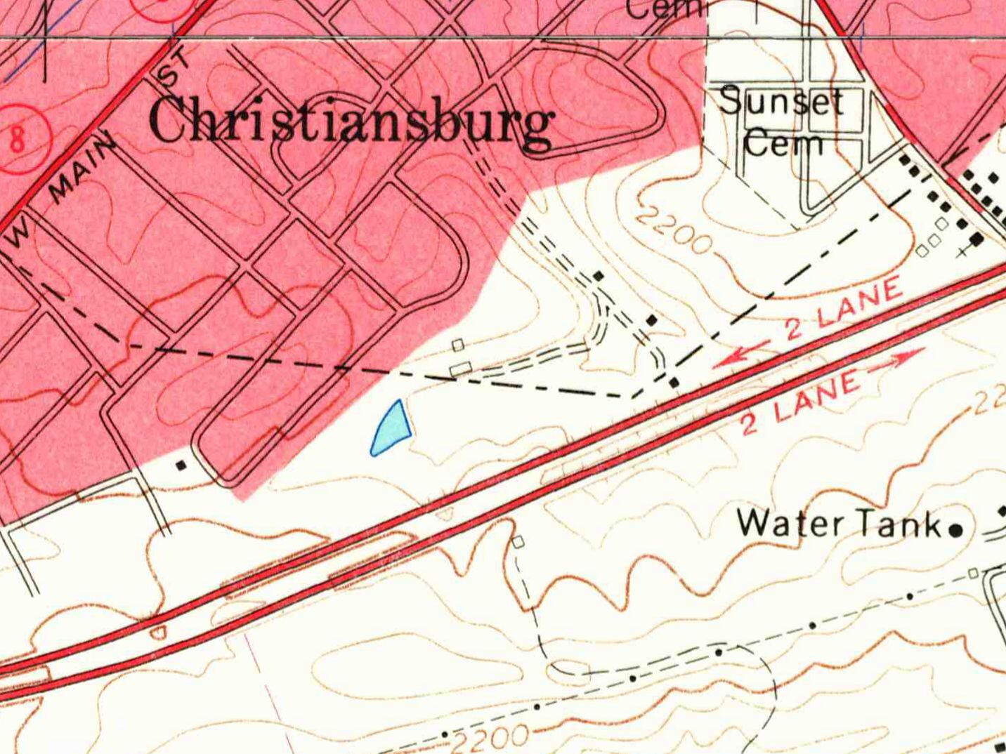 Detail of a 1965 topographic map: the pink built-up area of Christiansburg with its street grid at upper left, Sunset Cemetery labeled at top center, a double-dashed farm lane with a few buildings running northeast from a small blue pond, a divided highway labeled 2 Lane in each direction across the middle, and a water tank to the lower right.