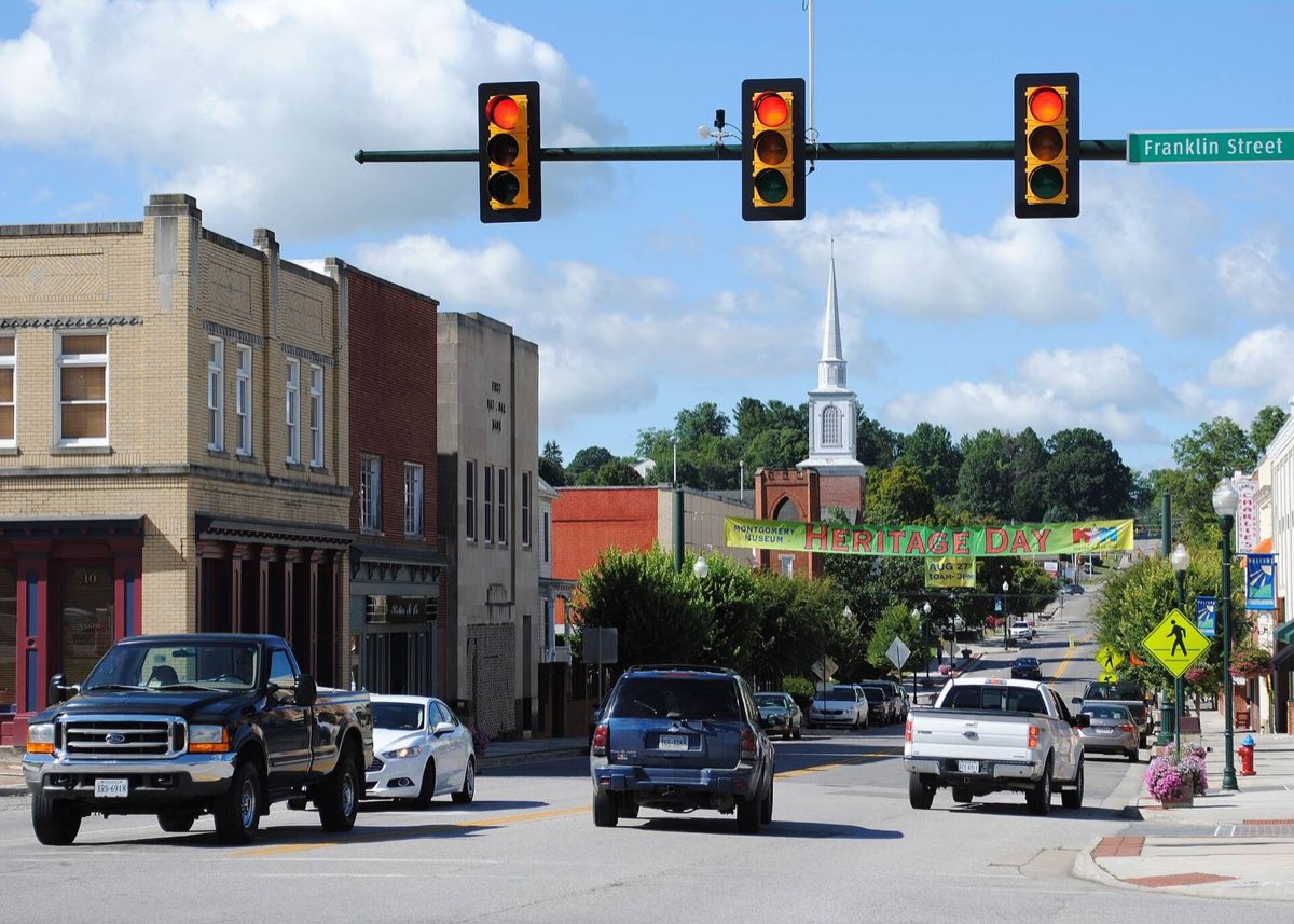 Main Street in downtown Christiansburg at the Franklin Street signal: brick storefronts, a white church steeple on the hill and a banner across the street